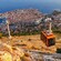 A cable car traveling up a steep mountain near a medieval town and coastline